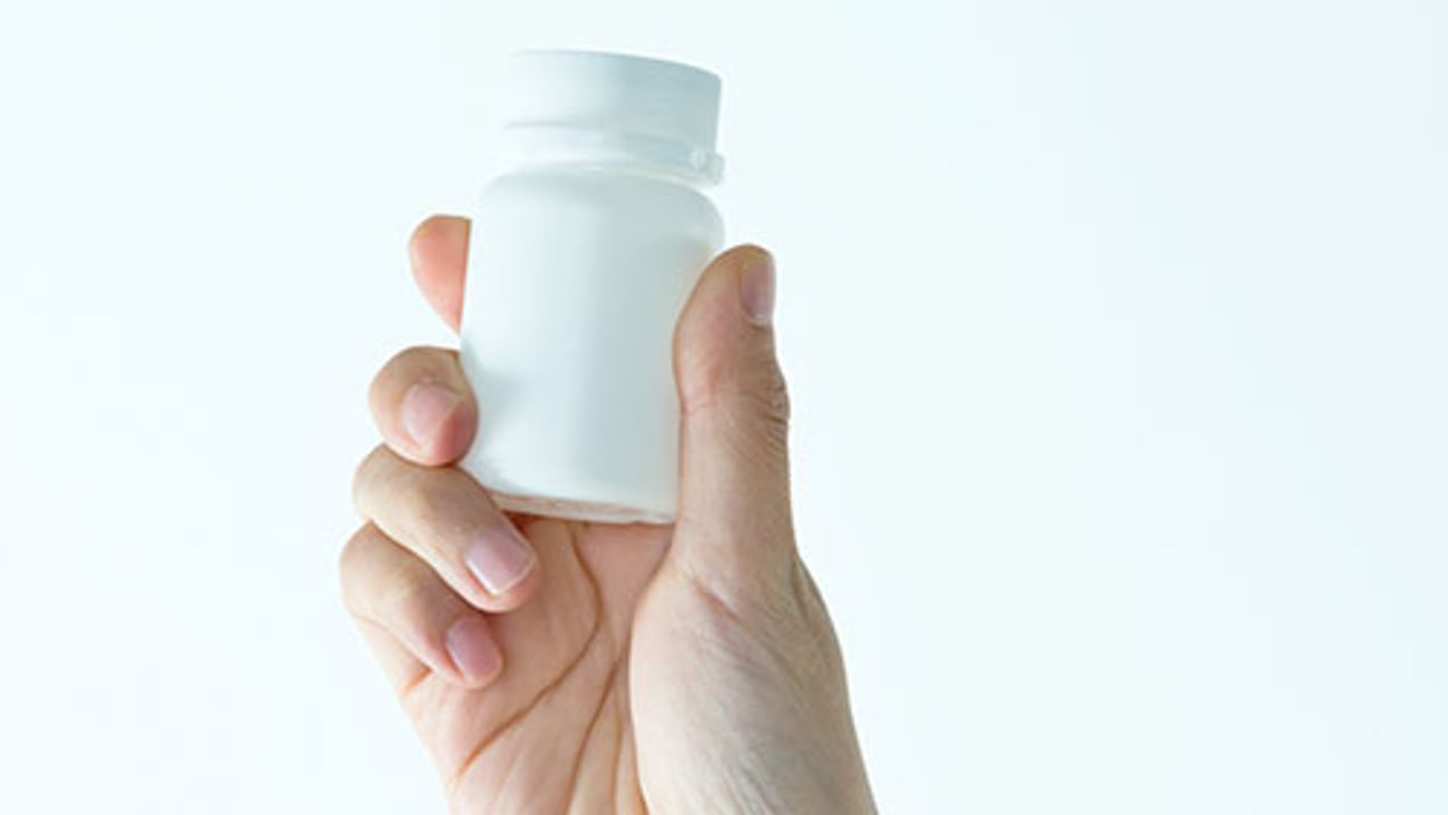 A hand holding a white pill bottle.