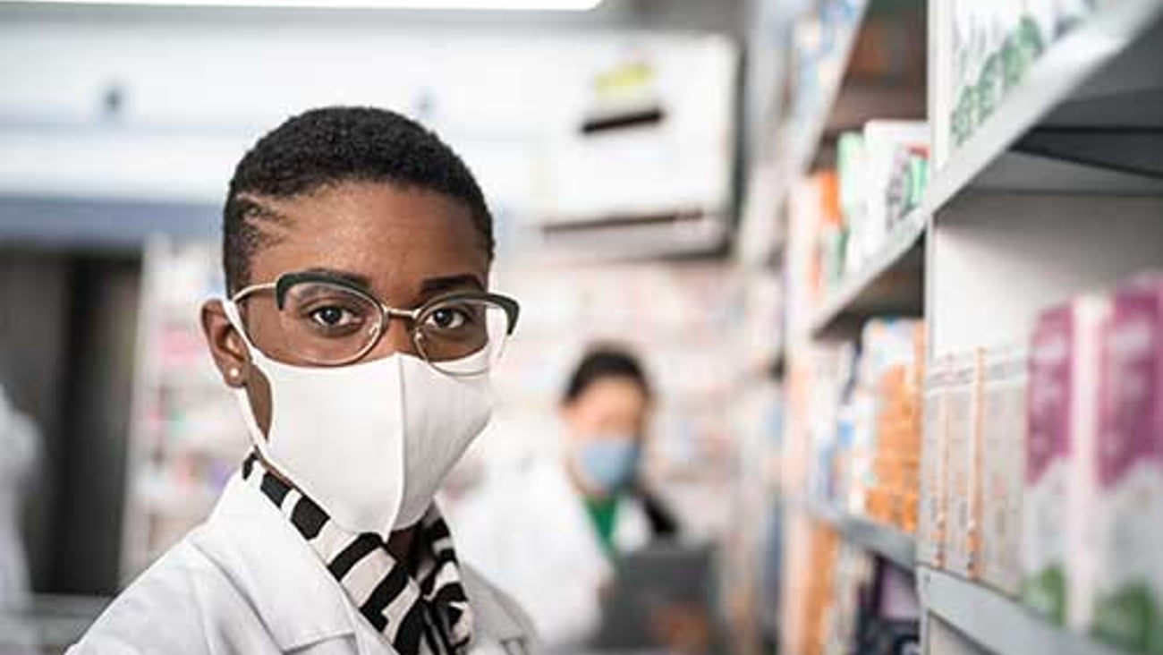 A male pharmacist wearing a mask and an employee behind him.