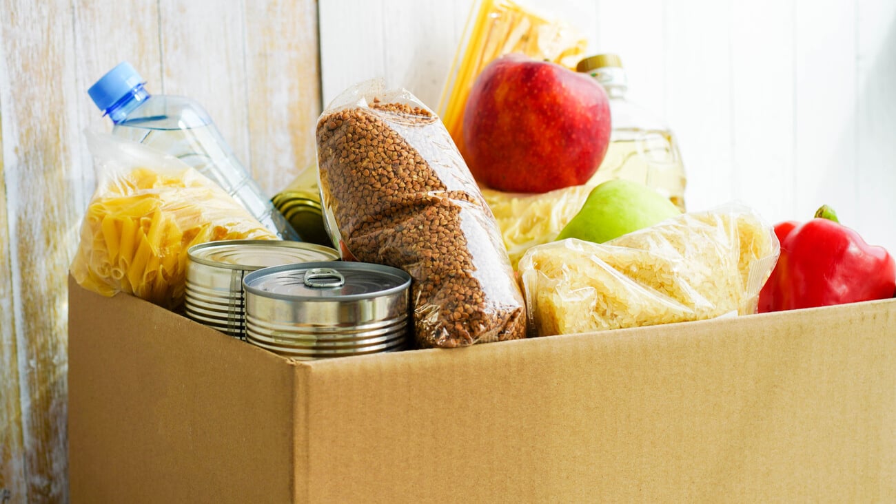 Donation box with various food. Open cardboard box with butter, canned goods, cereals and fruits.; Shutterstock ID 1718049334