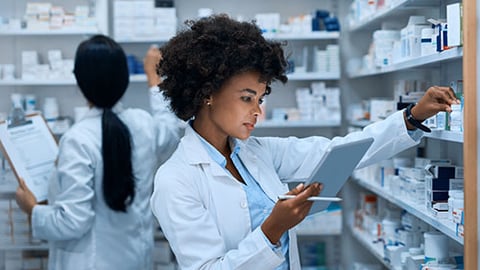 Two pharmacists in stock room with pill bottles.