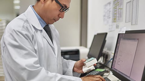 A male pharmacist typing at a computer. 