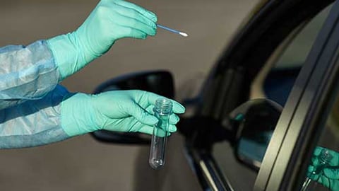 Gloved hands giving COVID-19 test to someone in a car.