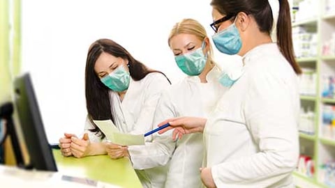 Three female pharmacists wearing masks.