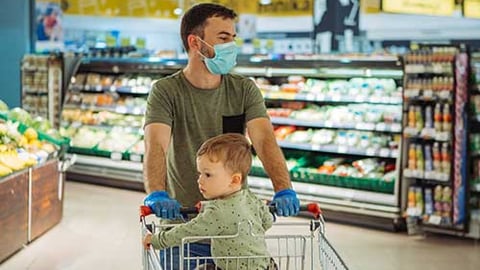 Father wearing mask with baby in supermarket cart. 