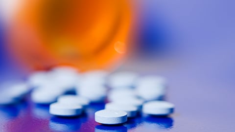 Out of focus pill bottle on its side with white tablets spilled out. 