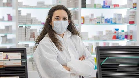 A pharmacist in a mask and white coat.