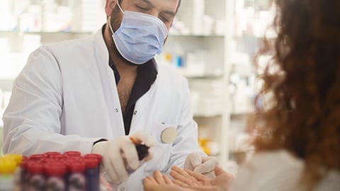 A pharmacist with a mask spraying sanitizer on patient.