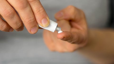 A person's hands dispensing a topical gel.