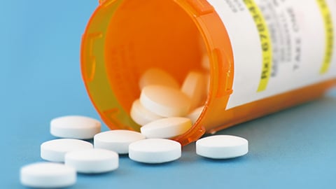 White tablets spilling out of a pill bottle against a blue background.