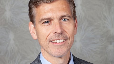 a man wearing a suit and tie smiling at the camera