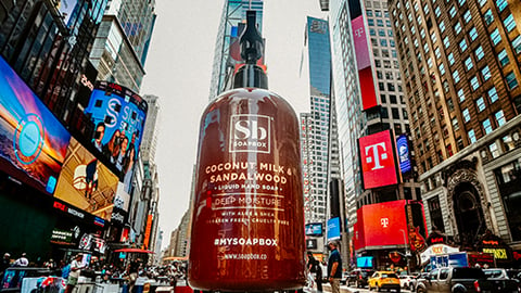 a person riding a skateboard down a street next to tall buildings with Times Square in the background