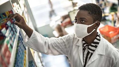 A pharmacist wearing a mask taking a medicine off shelf.