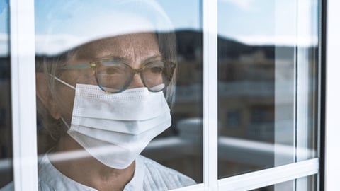 Women standing behind window wearing a mask