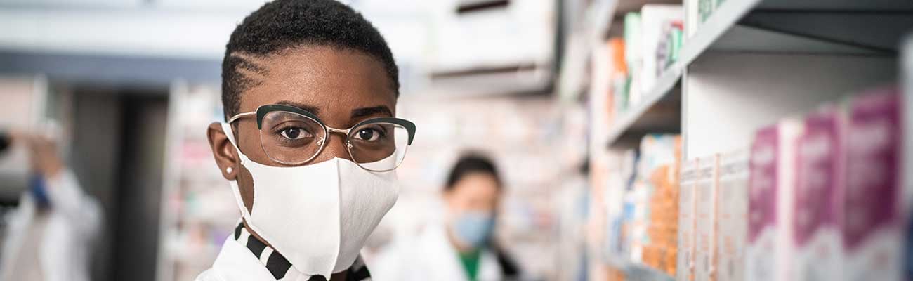 A pharmacist in a mask with a staffer in the background. 