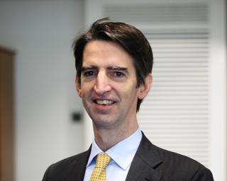 a man wearing a suit and tie smiling at the camera